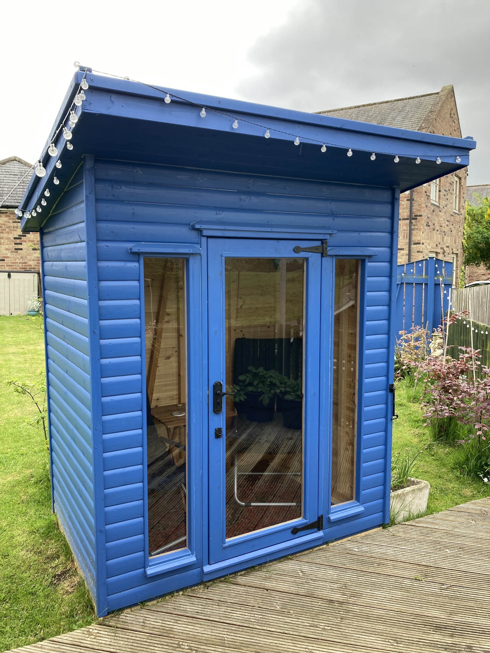 Bright blue pent summer house with glazed double doors on decking