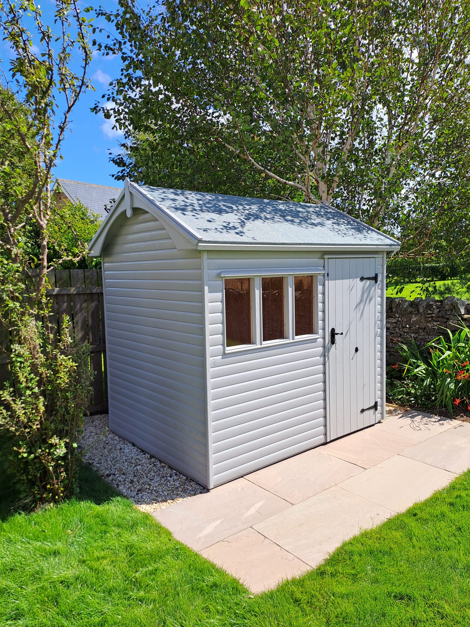 Pale grey apex shed on a paved base in a garden
