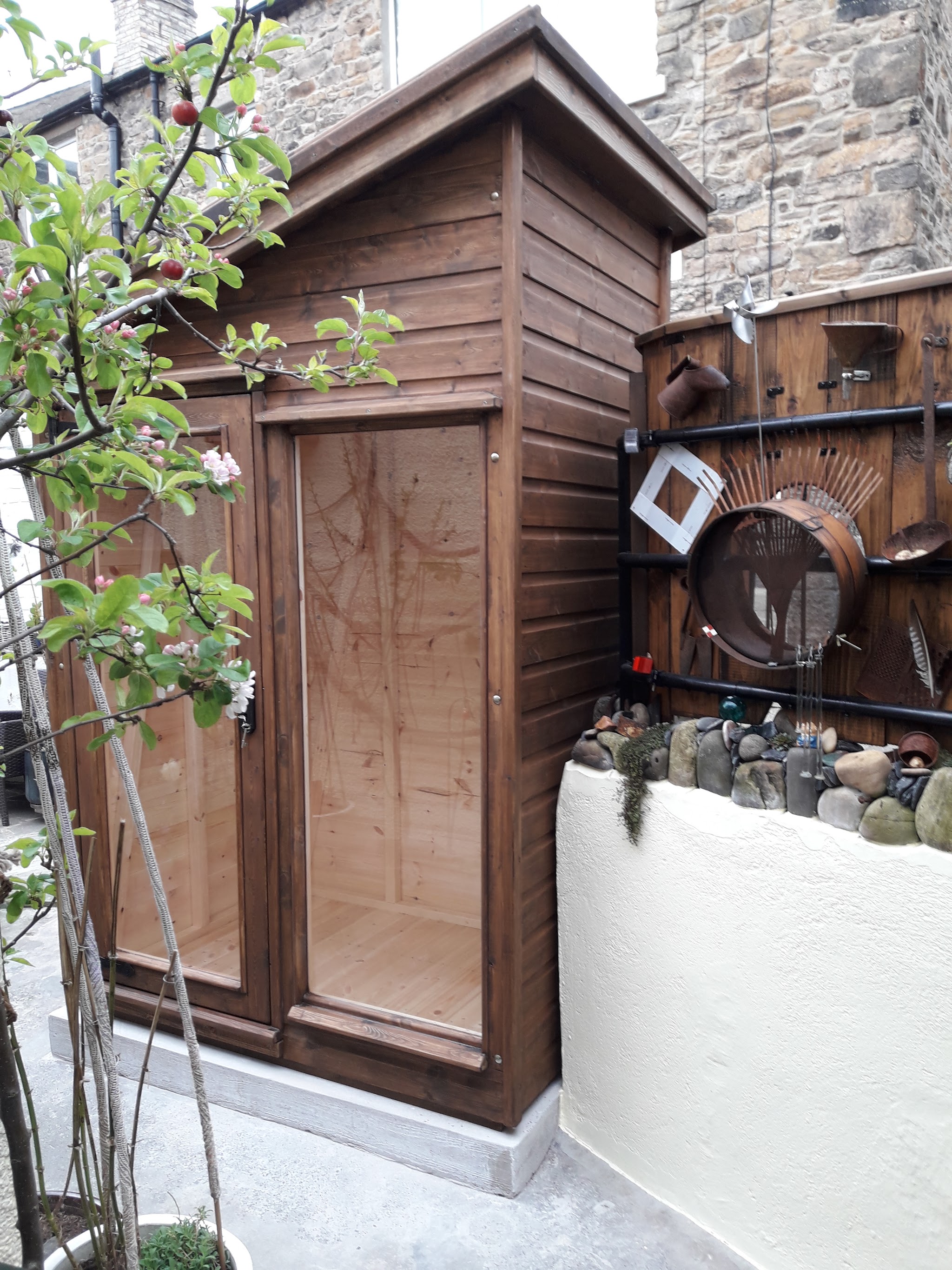 Tall dark stained shed against a stone cottage wall