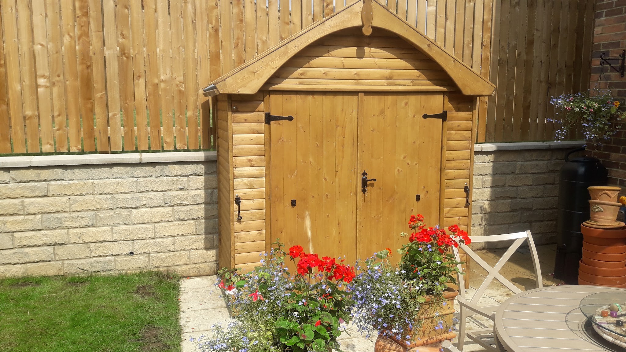Arched roof garden store with double doors beside geraniums