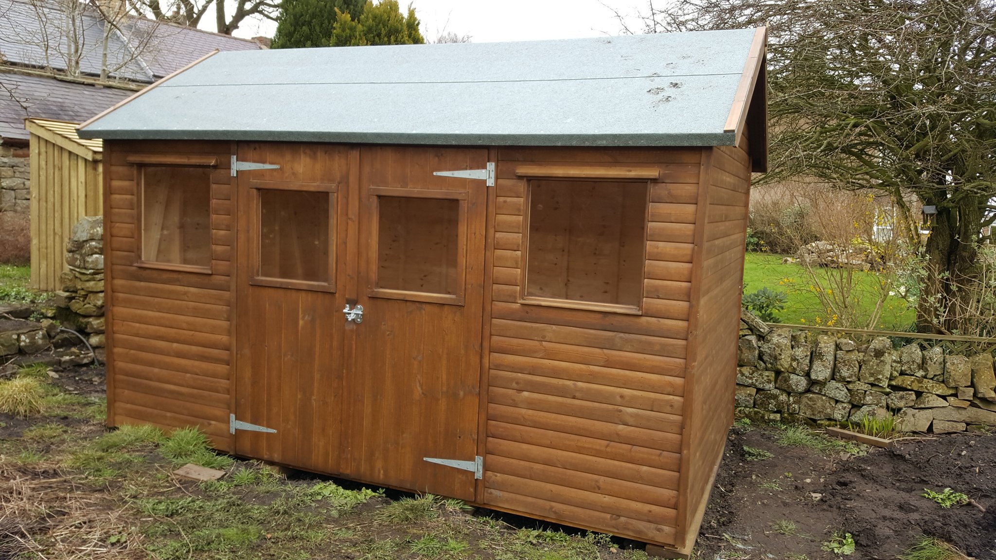 Large stained workshop shed with double doors beside a stone wall