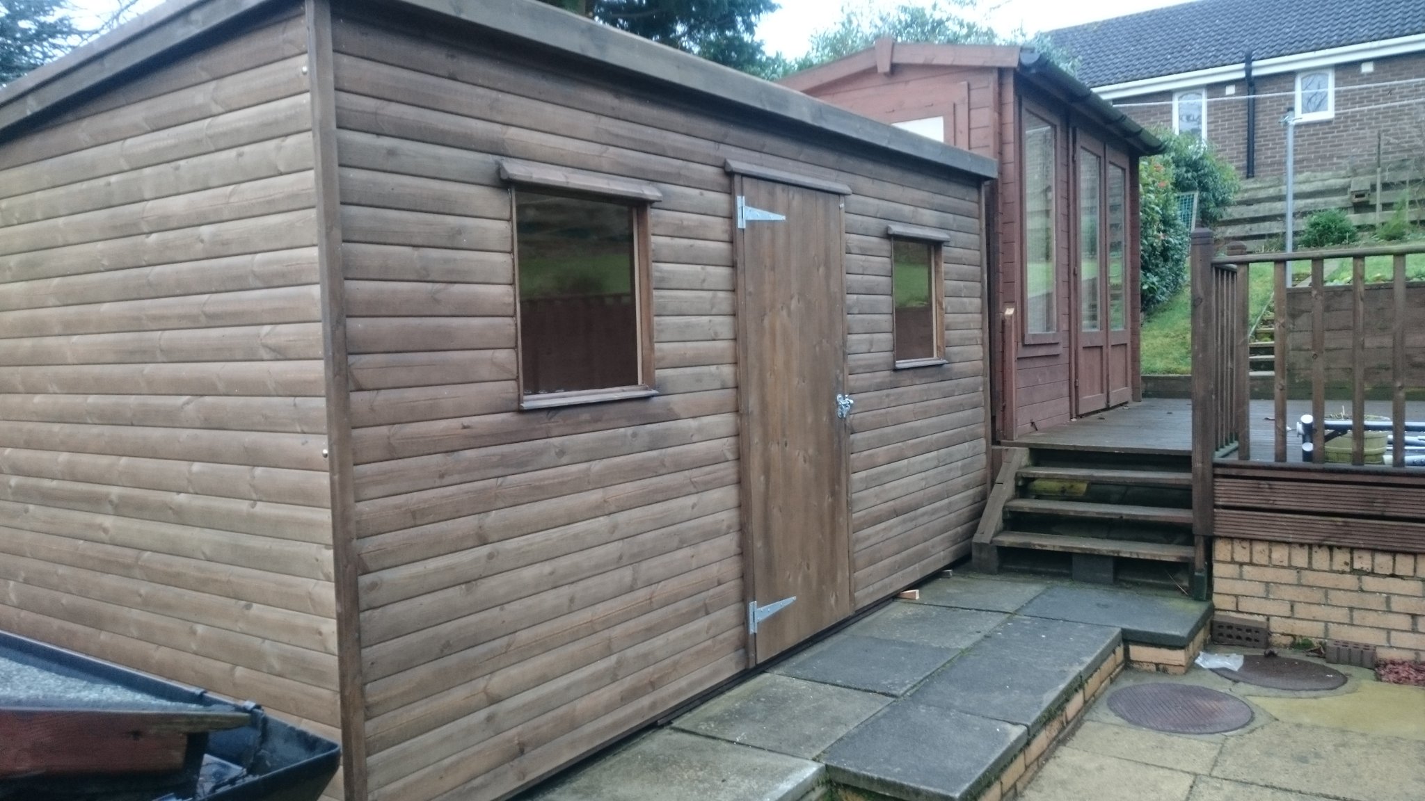 Long stained garden building beside a deck and steps