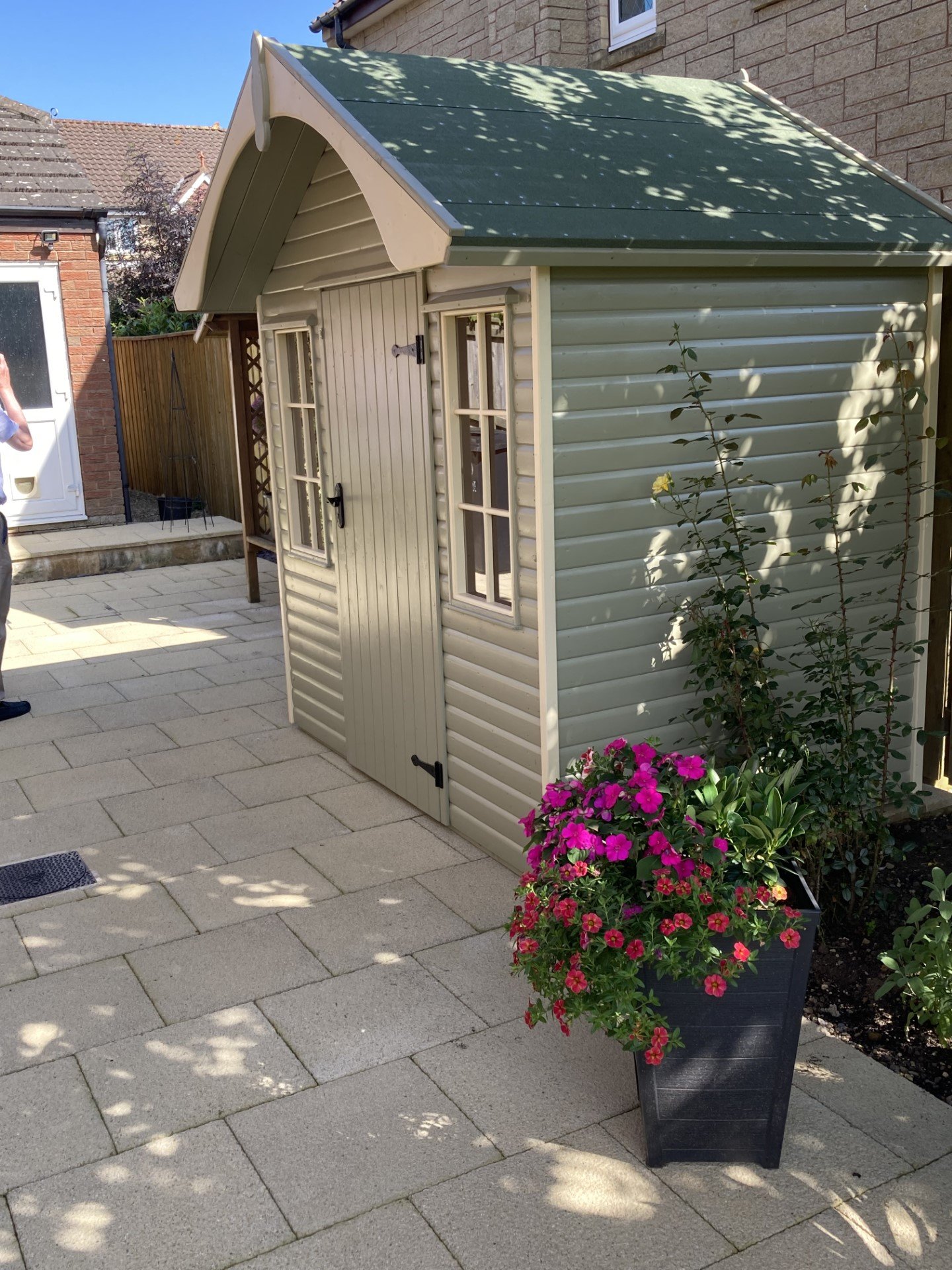 Sage painted shed with an arched bargeboard on a stone patio