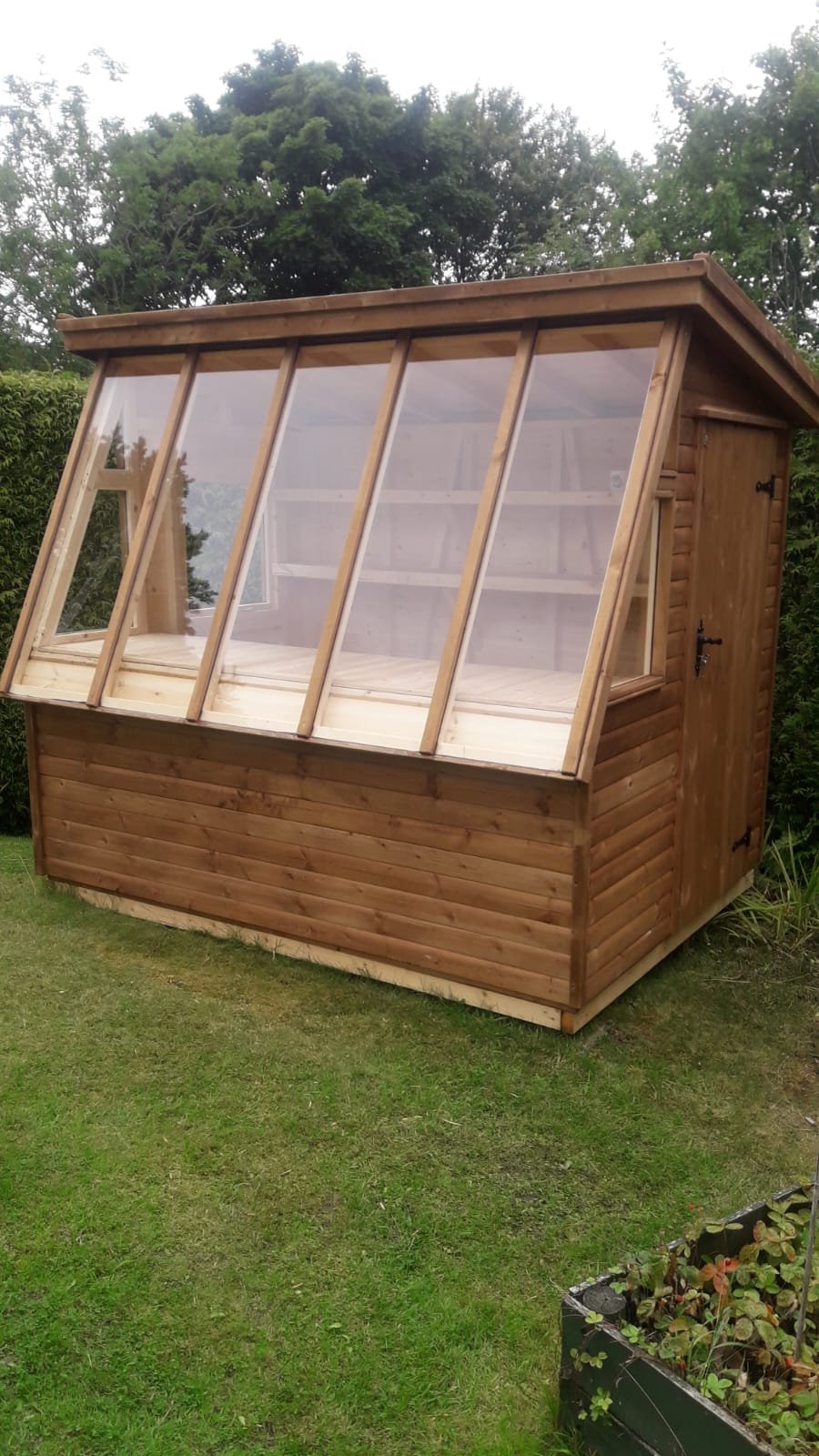 Potting shed with a long glazed slope on a lawn