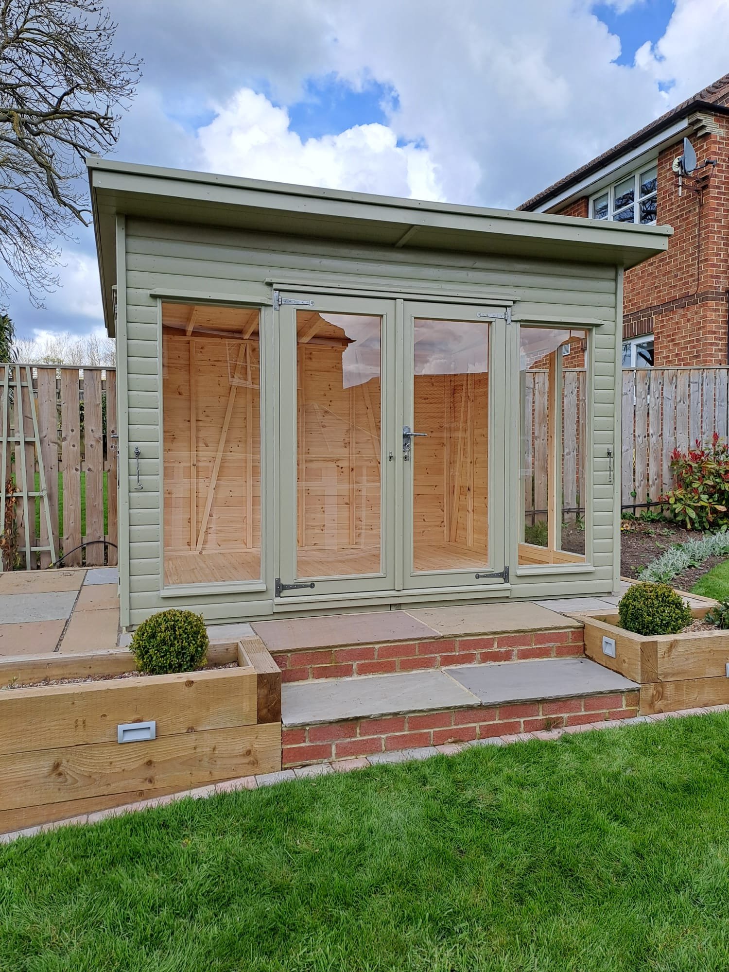 Sage pent summer house with glazed doors in a landscaped garden